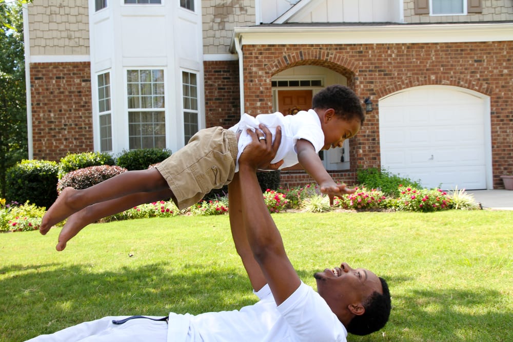 Dad holding up son in front yard of their house