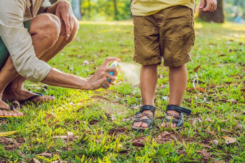 Parent applying mosquito spray on child’s legs in backyard for mosquito control and prevention