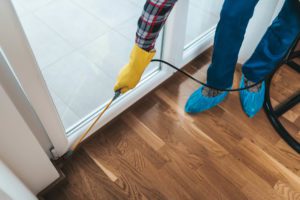 Professional exterminator in protective workwear spraying pesticide in apartment kitchen in the winter.